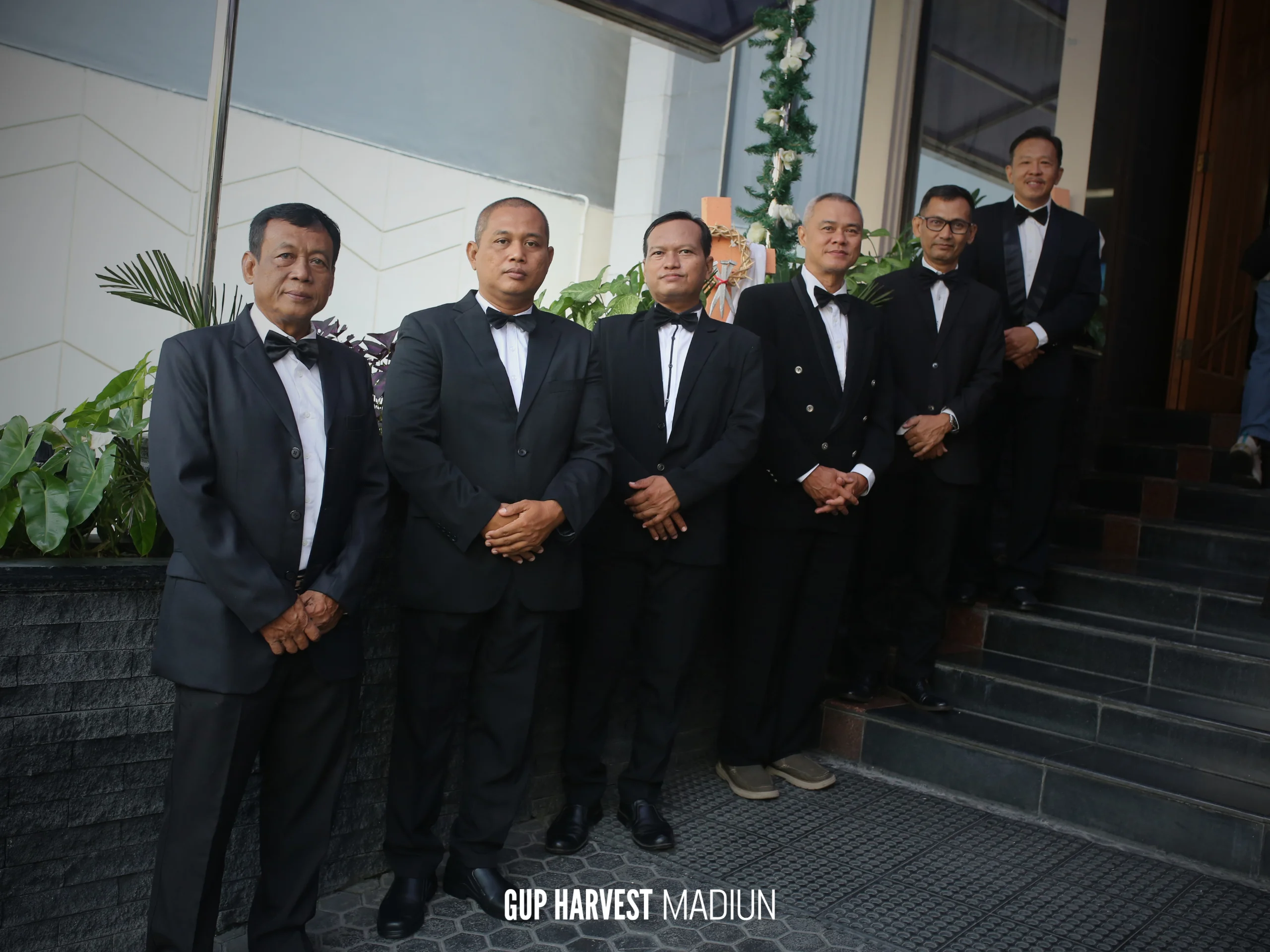Tim penyambut tamu pria berseragam jas formal bersiap menyambut jemaat di tangga masuk gereja.