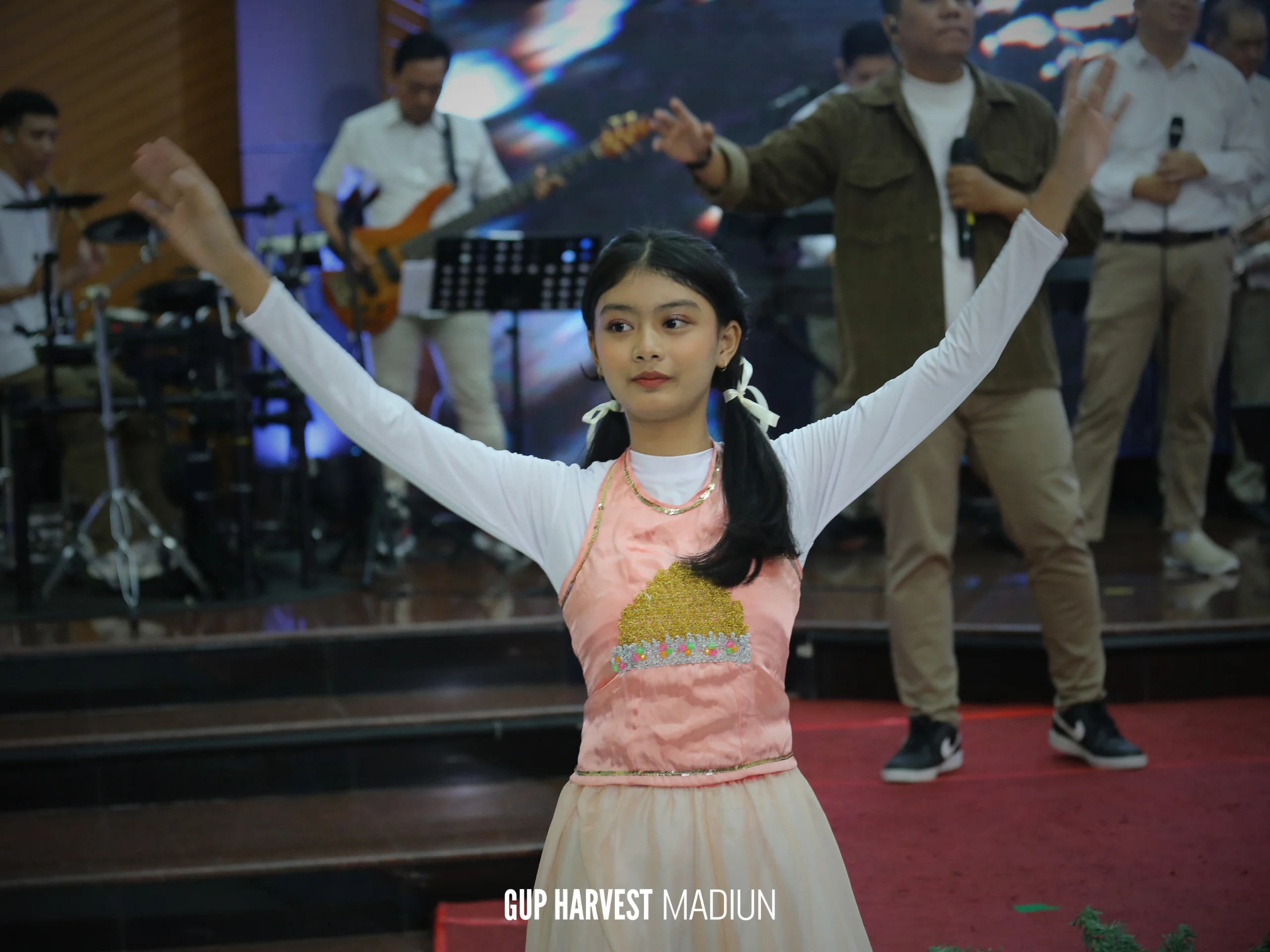 Penari anak mengangkat tangan dalam gerakan tarian penyembahan di atas panggung gereja.