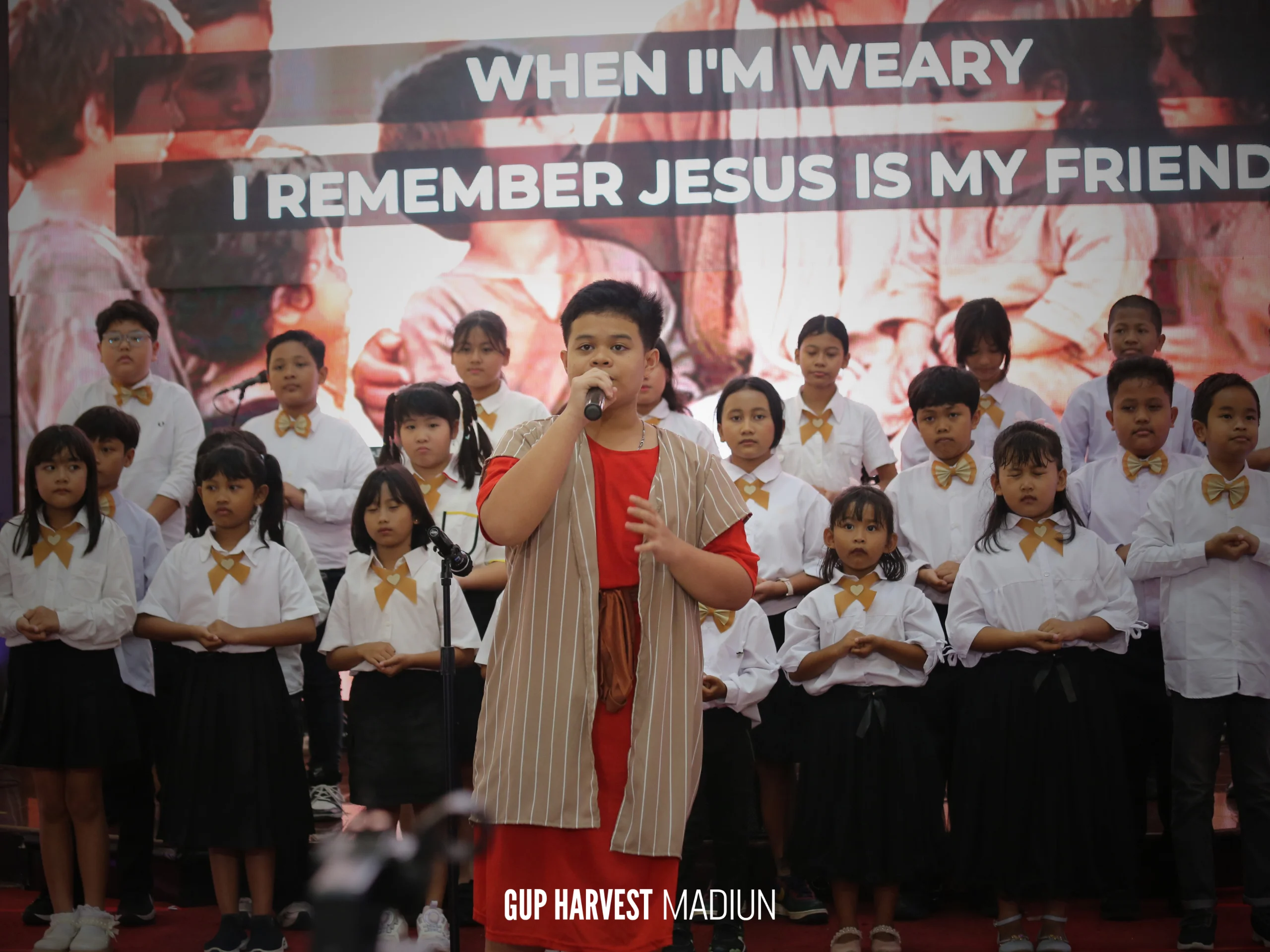 Seorang anak laki-laki berkostum alkitabiah menjadi solois, memimpin pujian bersama paduan suara Sekolah Minggu.