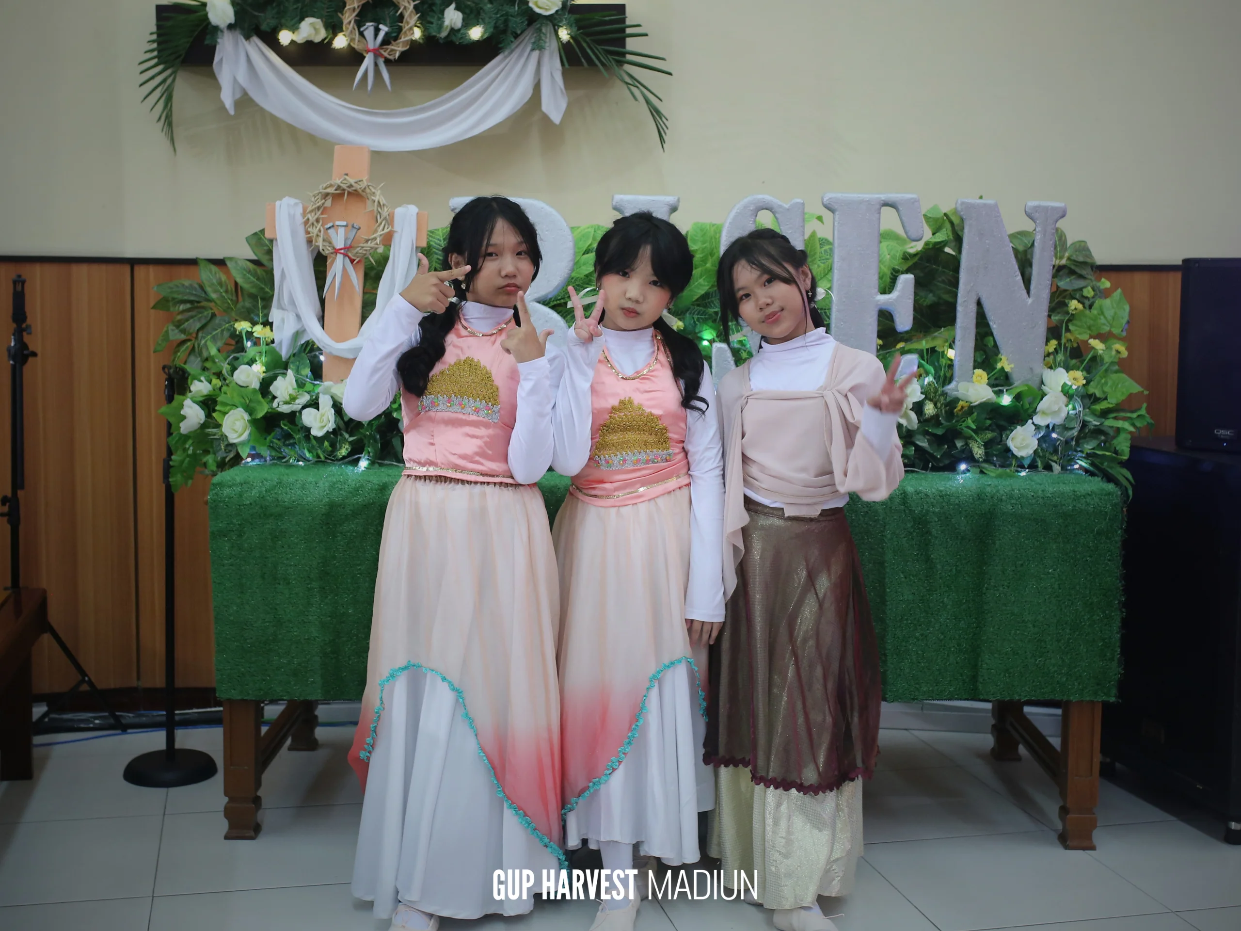 Potret manis penari cilik gereja berpose di depan dekorasi bertuliskan "He Is Risen" pada momen Paskah.